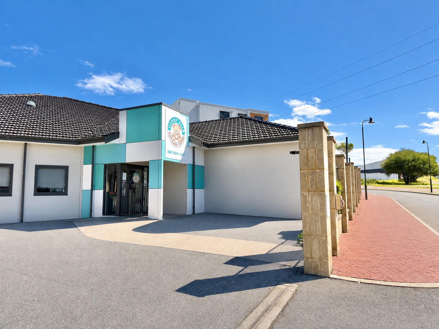 The entrance to Cuddly Bear Day Care Centre, with its teal and white panelled porch, the bear logo sign above the doors and the paved forecourt out the front.