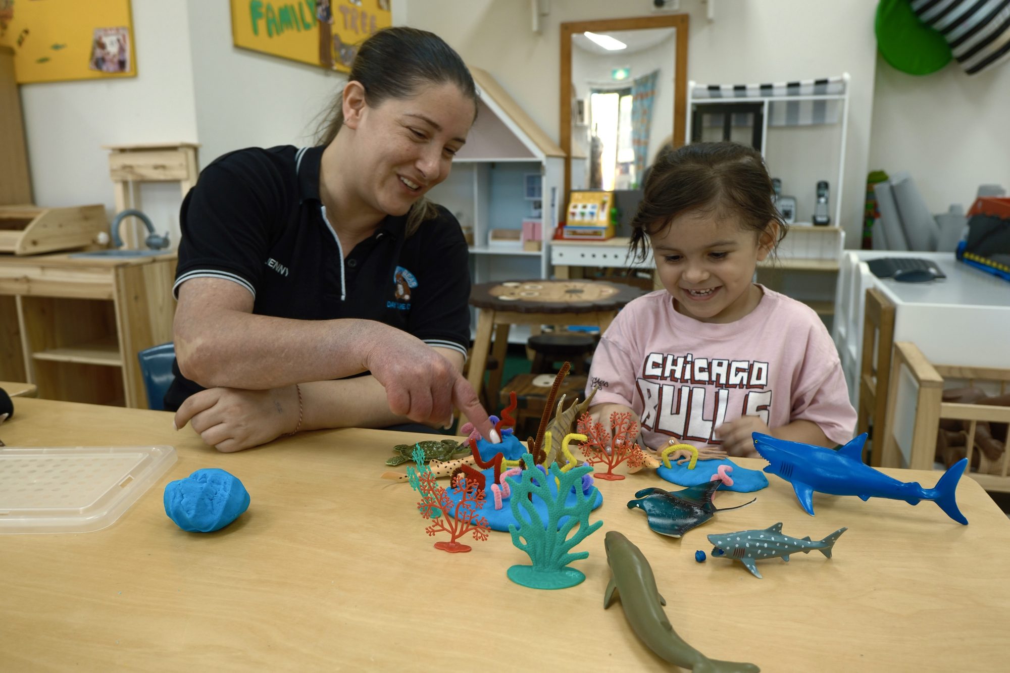 An educator and a child playing with playdough and toy sea creatures at a table