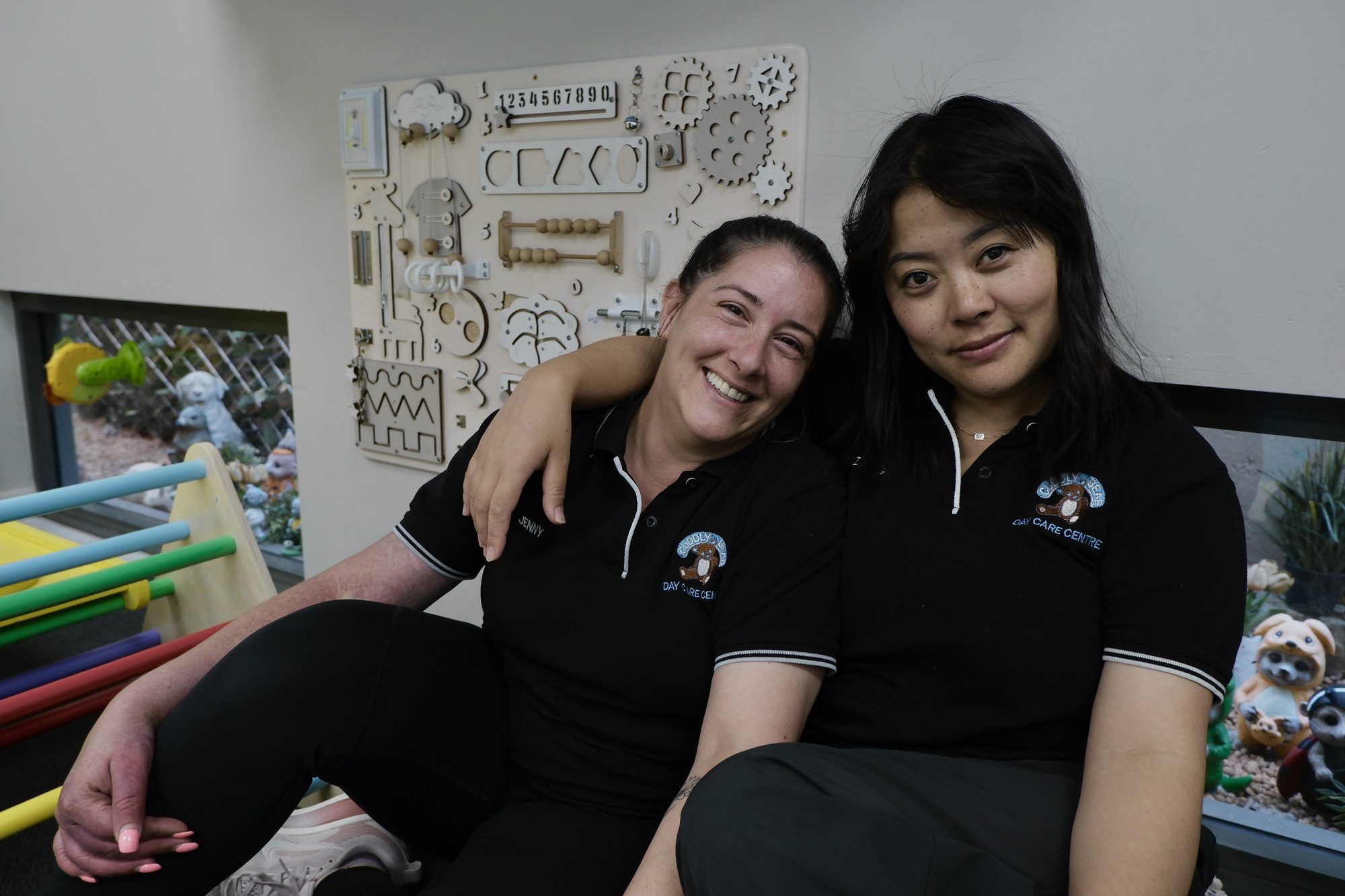 Two Cuddly Bear educators sitting arm in arm in their centre uniforms