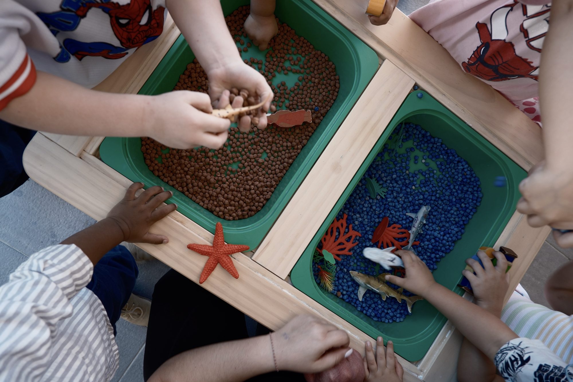 Children exploring sensory tubs of coloured beads with toy sea animals